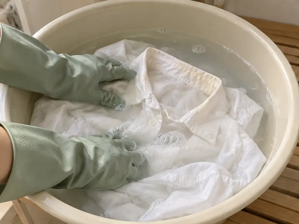 고무장갑을 낀 손으로 대야 속 흰 셔츠를 부드럽게 눌러 불리는 모습